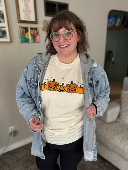Person wearing a white t-shirt with pumpkin design and denim jacket in a living room.